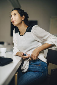 Thoughtful businesswoman injecting insulin while sitting on chair at table