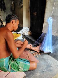 A  young man sitting outdoors and create fishing net..