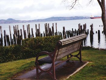 Deck chairs on grass by lake against sky