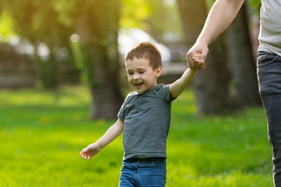 Happy three year old toddler boy walks hand in hand with dad in the park on a sunny spring day. 