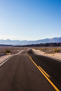 Road leading towards mountains against clear sky