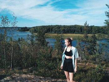 Full length of young woman standing by lake against sky