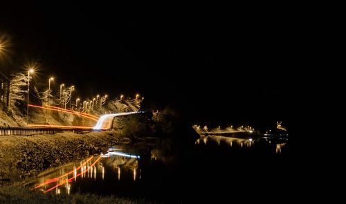 Illuminated light trails over lake against sky at night