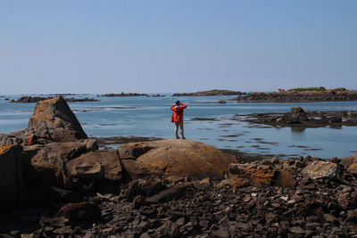 Man standing on rock by sea against clear sky