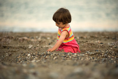 Adorable toddler baby playing on a beach with pebble stones.