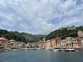 Sailboats moored in sea by townscape against sky