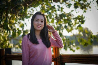Portrait of young woman standing against trees