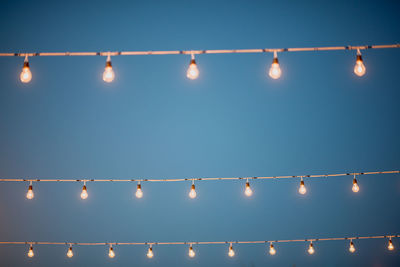 Low angle view of illuminated light bulbs against clear blue sky