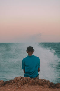 Rear view of man looking at sea against clear sky during sunset