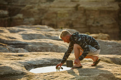 Man in camo jacket collects cooking water from a shallow puddle