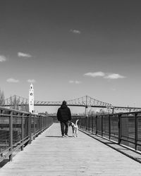 Rear view of man walking on footbridge against sky