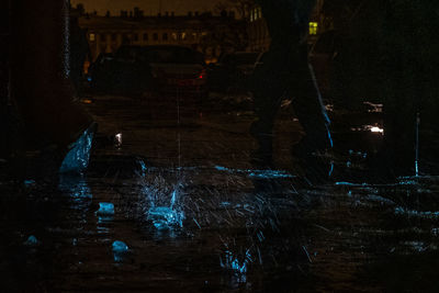 Low section of person standing by illuminated water at night