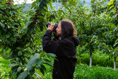 Rear view of man photographing woman against plants