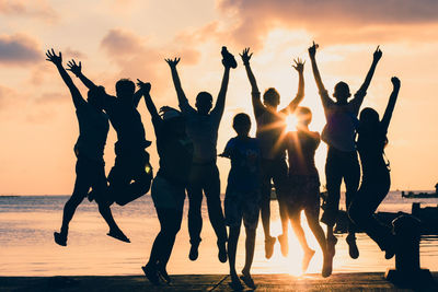 Silhouette friends jumping at beach during sunset