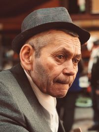 Close-up of man wearing hat looking away while sitting outdoors