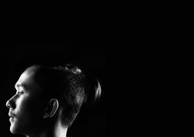 Close-up portrait of boy looking away against black background