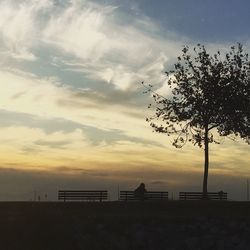 Silhouette of bench by sea against dramatic sky