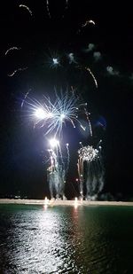 Firework display over sea against sky at night