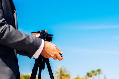 Midsection of man photographing while standing against blue sky