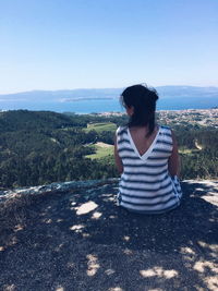 Woman sitting on mountain against clear sky