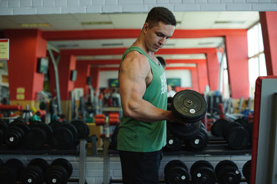 Side view of young man lifting dumbbell at gym