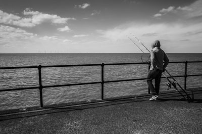 Rear view of man wearing hood while fishing in sea