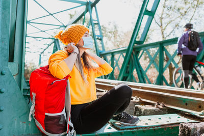 Woman wearing mask sitting on railway bridge