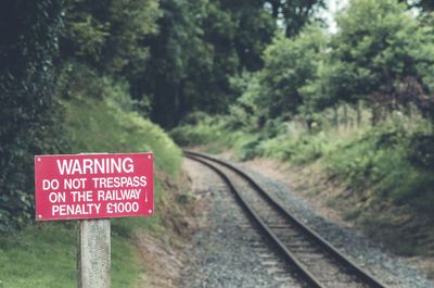 Red warning sign by railroad track against trees