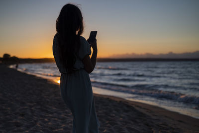 Silhouette woman standing at beach against sky during sunset