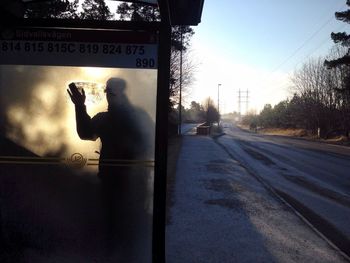 Shadow of man on bus stop glass by empty road during winter