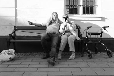 Man and woman taking selfie on bench against building