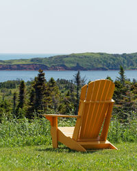 Chair on field by lake against sky