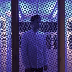 Young man seen through metal grate at night