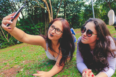 Female friends taking selfie while lying on grass at park