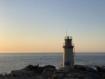 Lighthouse on rock by sea against sky during sunset