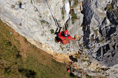 Aerial view of mountain rescuer abseiling on a rocky wall hanging on a rope