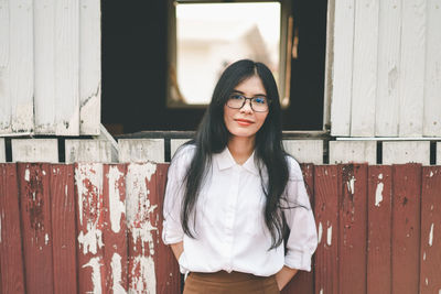 Portrait of smiling young woman standing against wall