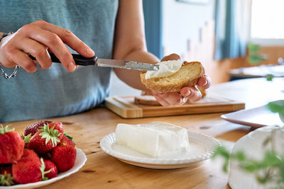 Female hands spread stracchino cheese on bread for toast. healthy eating, fruit dieting brunch.