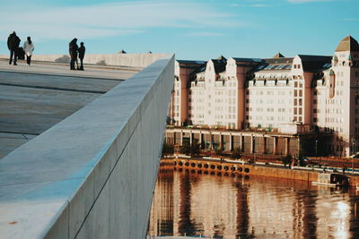 People on bridge over canal in city against sky