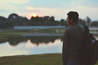 Rear view of man standing at beach against sky during sunset