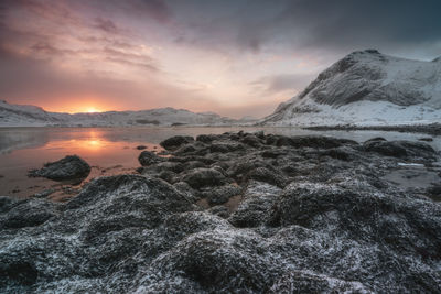 Scenic view of sea by snowcapped mountains against sky during sunset