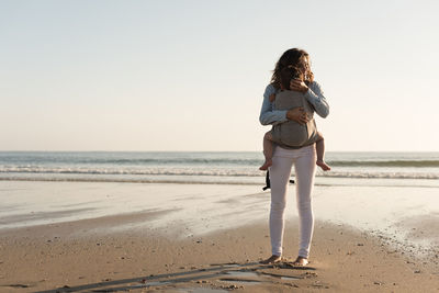 Mother carrying son while standing at beach