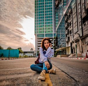 Portrait of woman sitting against buildings in city
