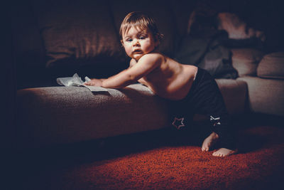 Portrait of shirtless baby boy standing by sofa at home