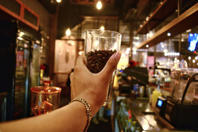 Cropped hand of woman holding glass with roasted coffee beans