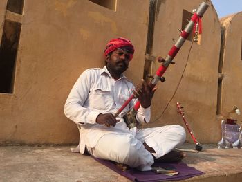 Contemplating man with musical equipment sitting against wall