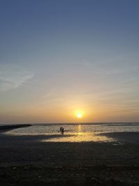 Silhouette people on beach against sky during sunset