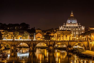 Illuminated ponte sant angelo bridge over tiber river against st peter basilica