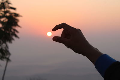 Optical illusion of cropped hand holding sun against sky during sunset