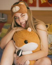 Portrait of happy young woman with stuffed toy sitting on bed at home